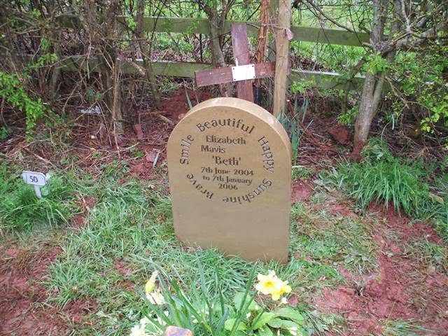 A rounded sandstone headstone in a natural woodland setting