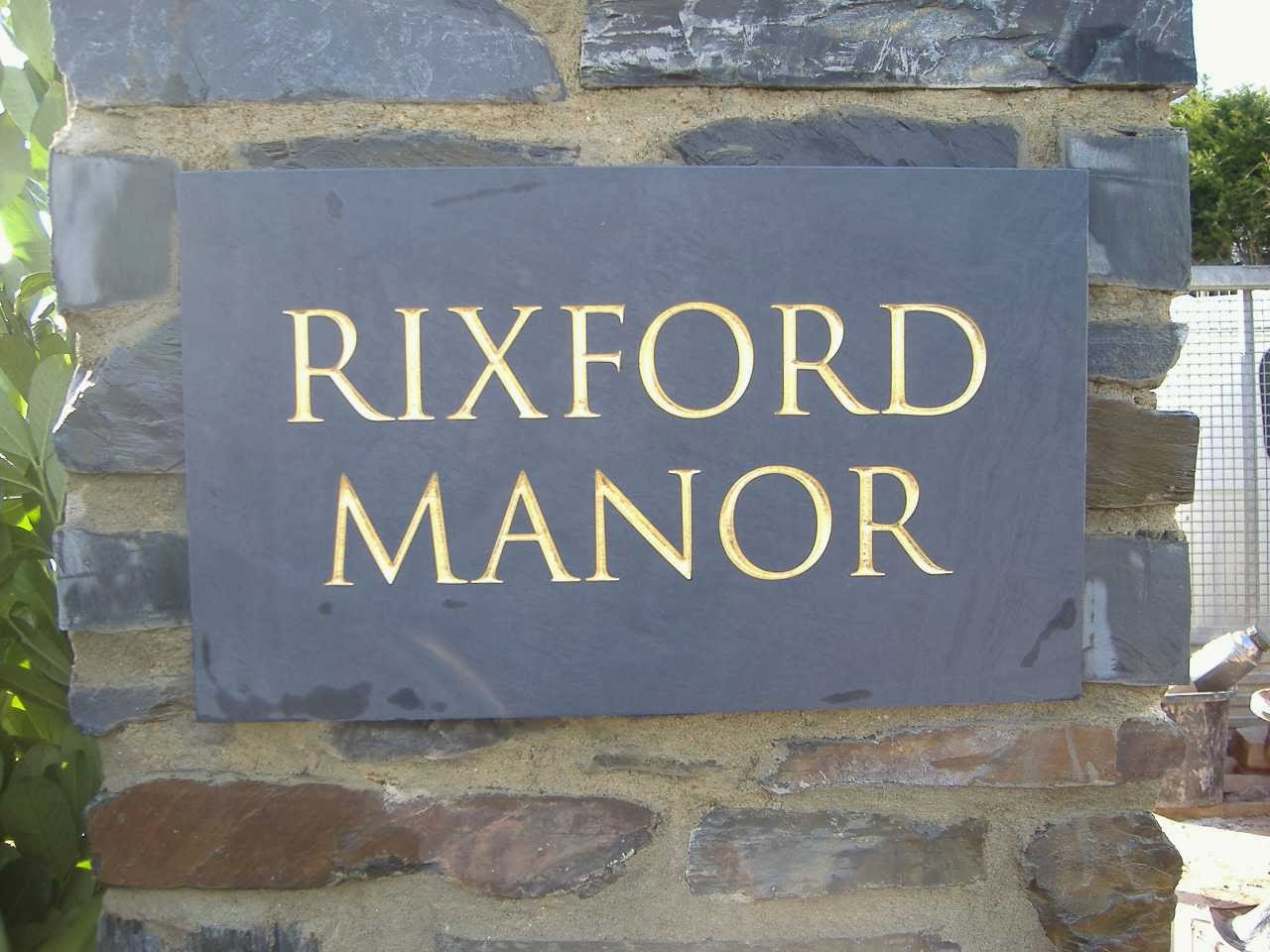 Slate house sign reading Rixford Manor with gilded letters, set into a stone wall